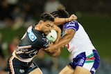 A Wests Tigers player tries to fend off a Warriors player with a hand top the shoulder as he carries the ball.