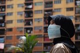 A woman in a hijab wears a mask in front of a high-rise building.