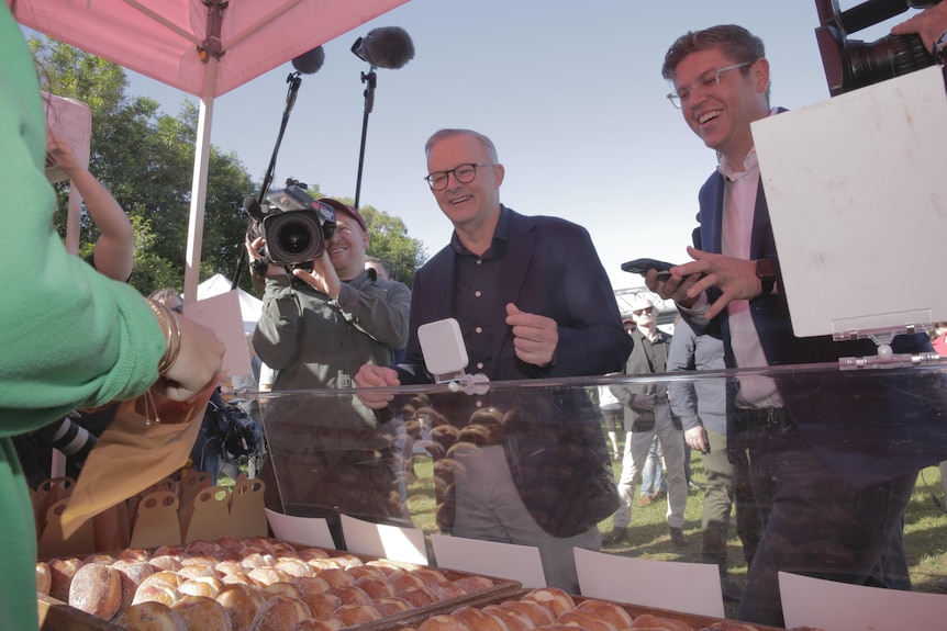 Labor leader Anthony Albanese stands at a doughnut stall alongside Bennelong candidate Jerome Laxale as cameras watch on
