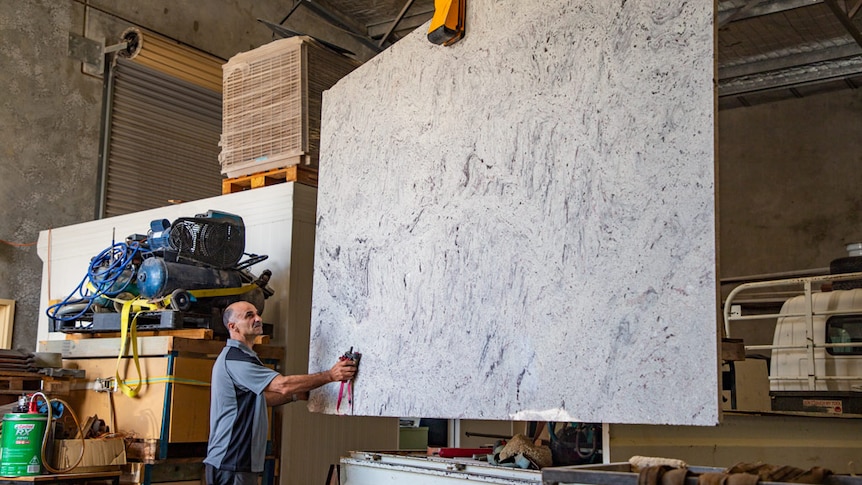 A man in a workshop touching a large piece of grey natural stone.
