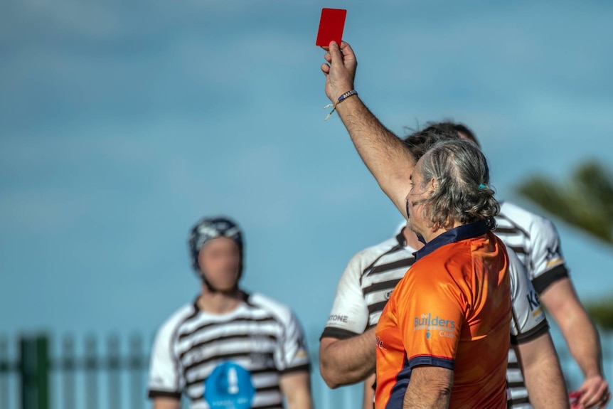 Man in orange shirt faces away and holds red card in the air