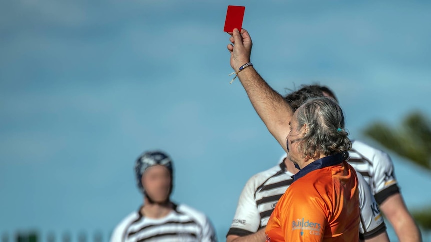 Man in orange shirt faces away and holds red card in the air