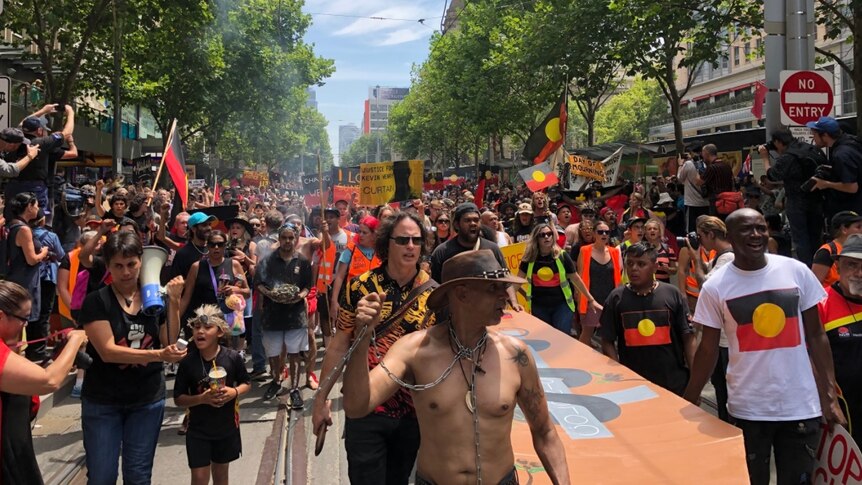 Invasion Day protesters walk in Melbourne with Aboriginal flags
