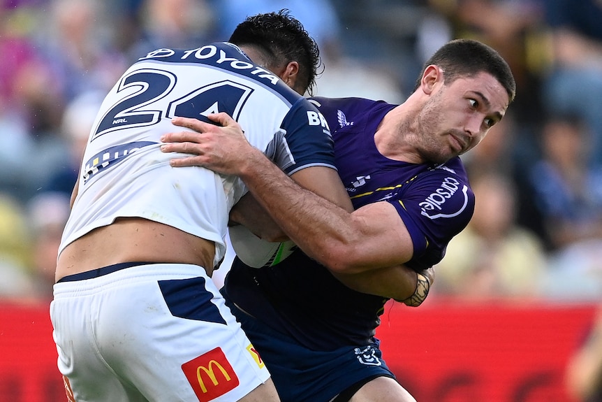 A Melbourne Storm NRL player holds the ball as he is tackled by a North Queensland opponent.