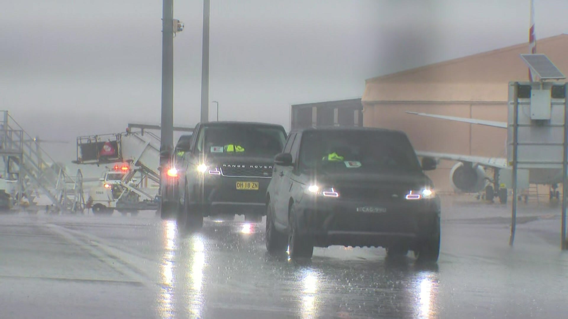 Cars drive in a line behind a chain link fence