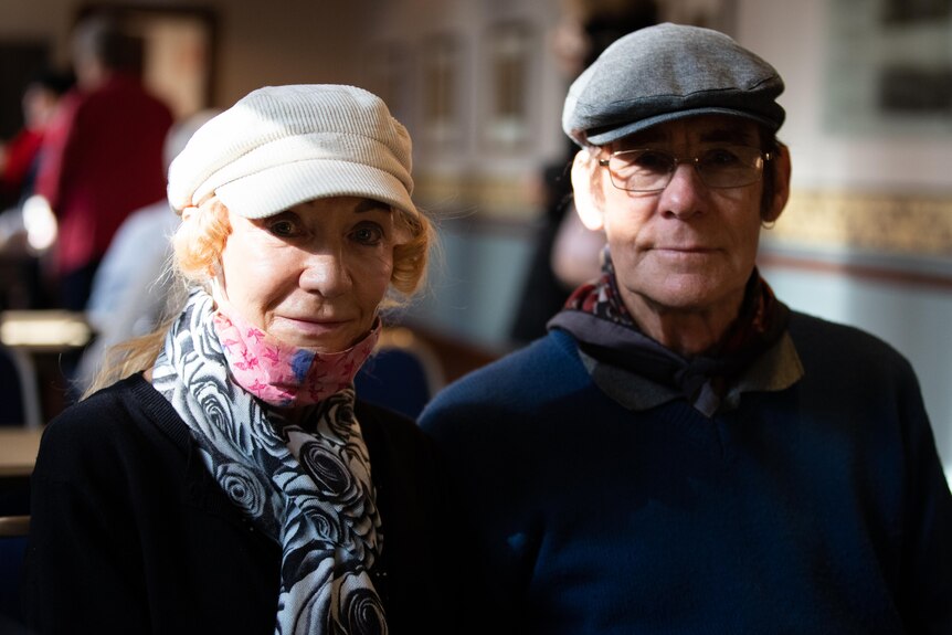 An older couple rugged up in a cafeteria drinking tea.