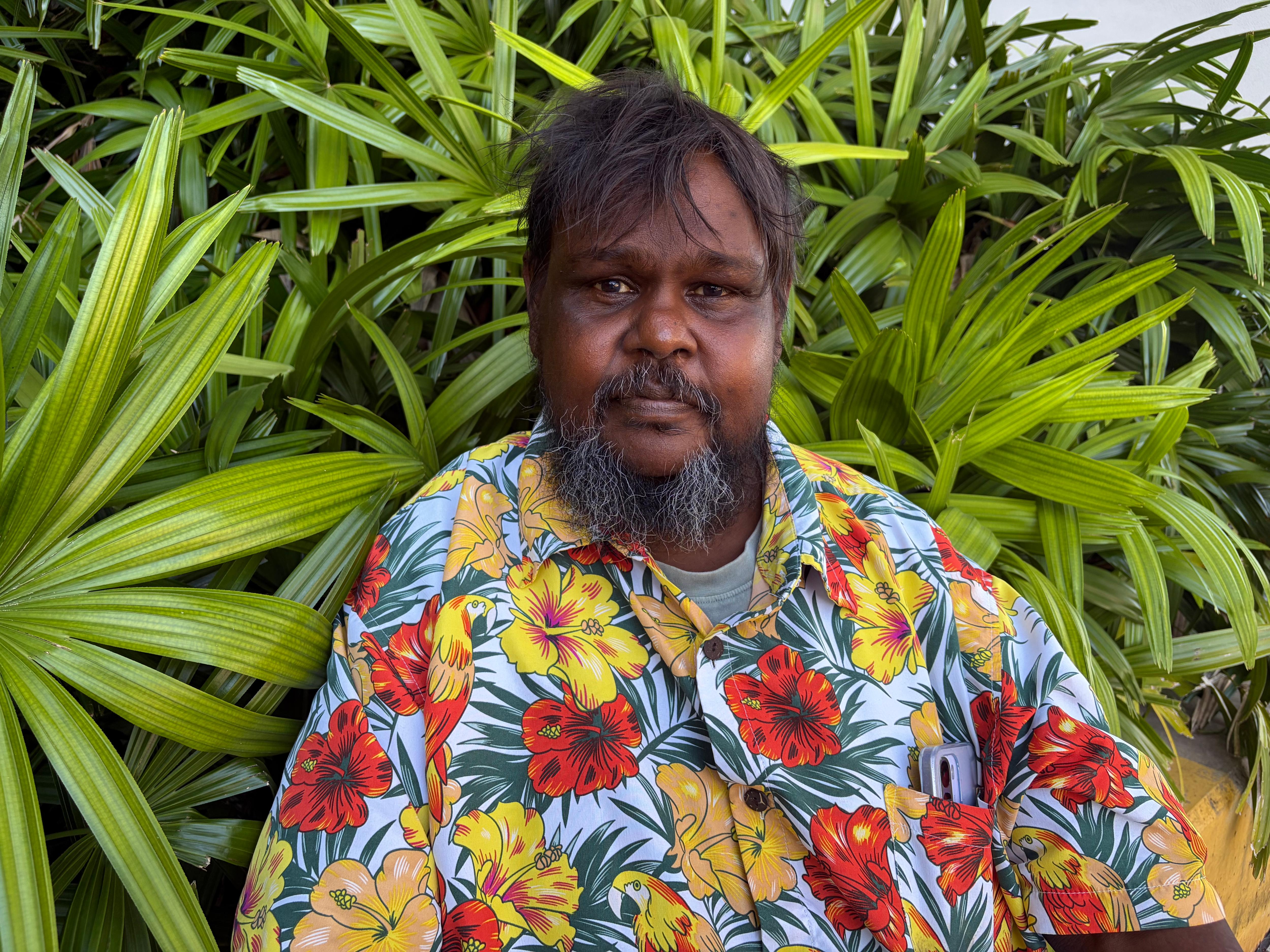 El hombre con camisa floral se para frente a plantas verdes 