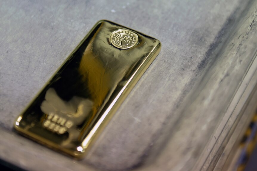 A gold bar stamped with Perth Mint's logo sits on a metal tray. Its surface is polished.