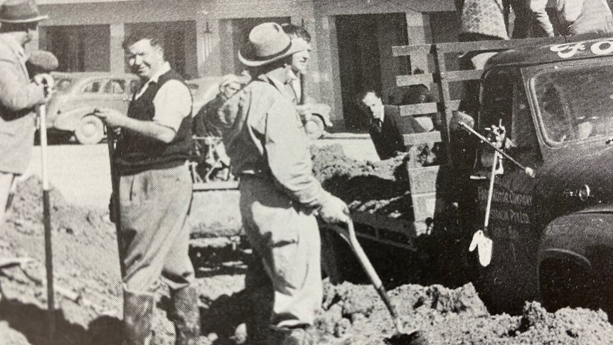 A black and white image of men with shovels standing in front of a hotel