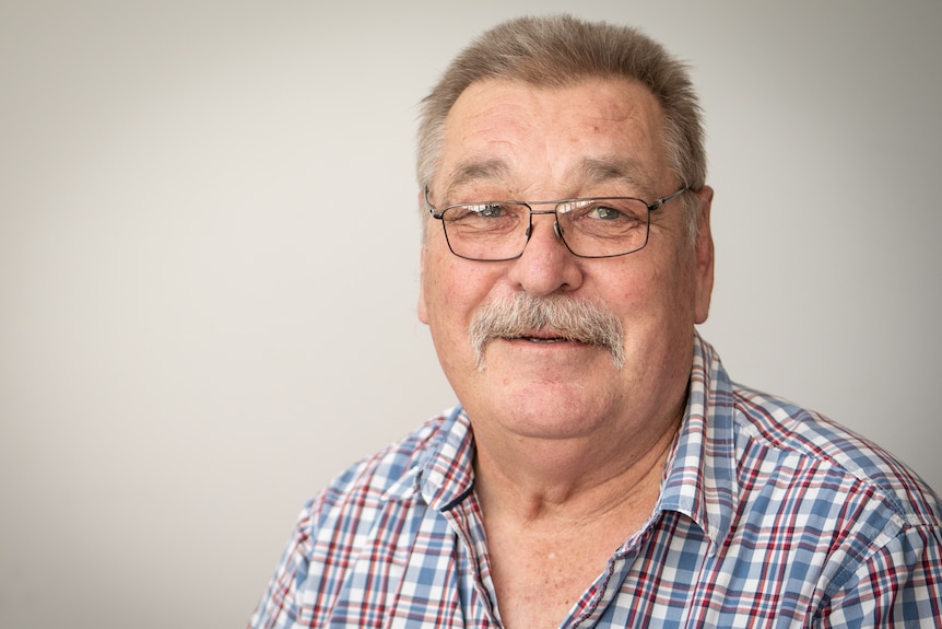 Head shot of older man with glasses and checked shirt.