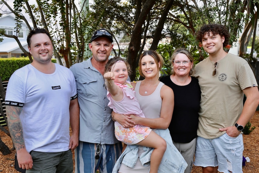 Three men and two women, one holding a young girl, all smiling.