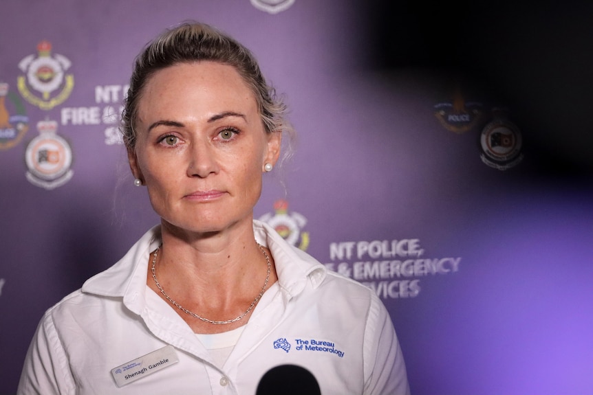 A woman standing in front of a camera, with a purple NT emergency services banner in the background.