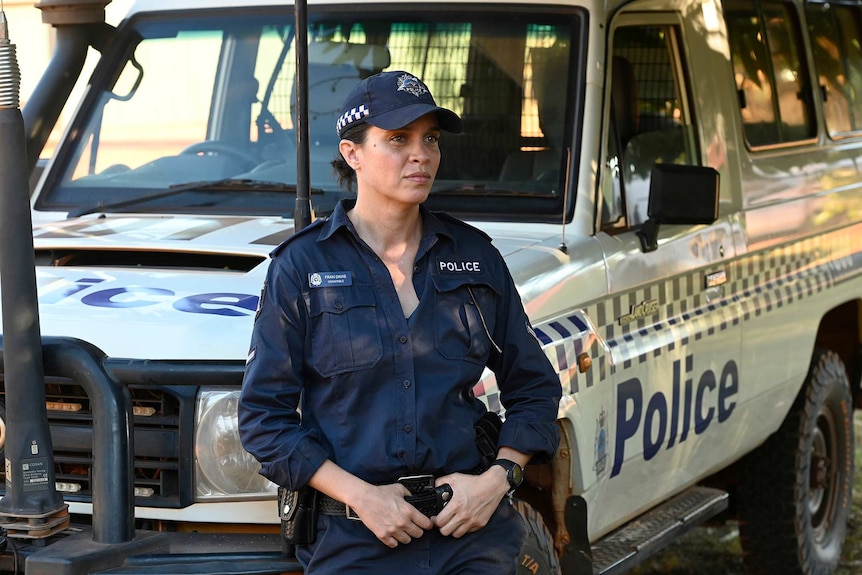 Jada Alberts as a police officer in the TV show Mystery Road, she leans against a police car