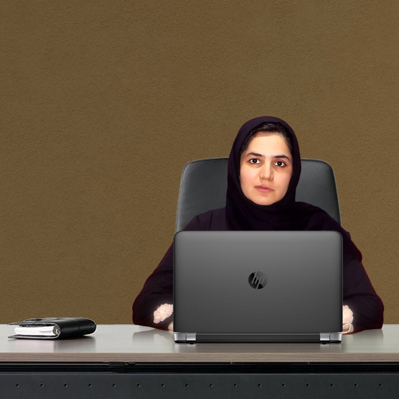 Sodaba Herari sits behind a desk dressed in black using a laptop.