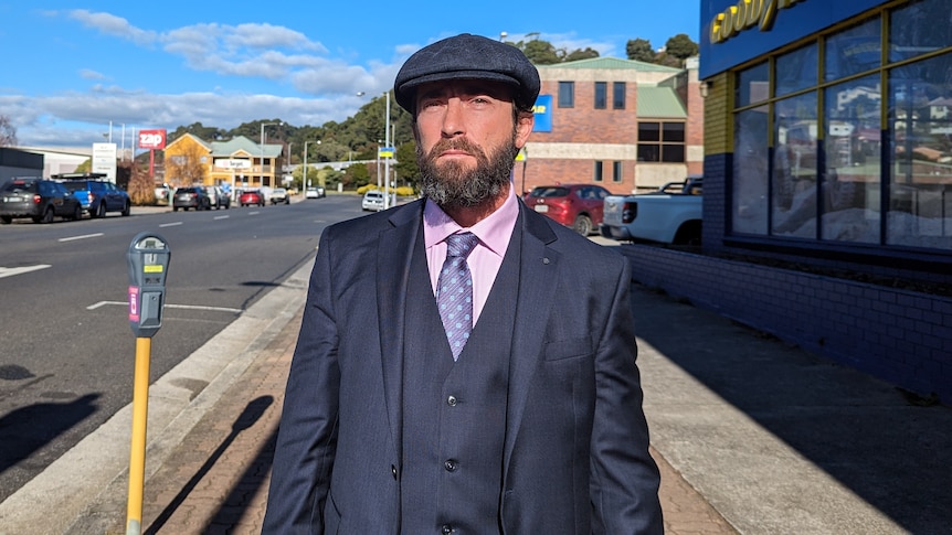 Daniel Victor Gandini, wearing a three piece suit and peak cap, standing in the sunshine on the street in Burnie.