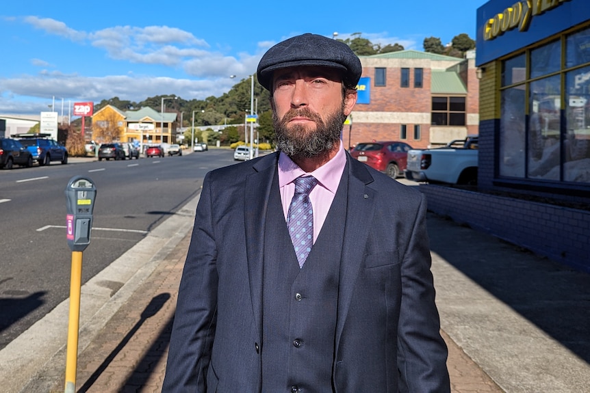Daniel Victor Gandini, wearing a three piece suit and peak cap, standing in the sunshine on the street in Burnie.
