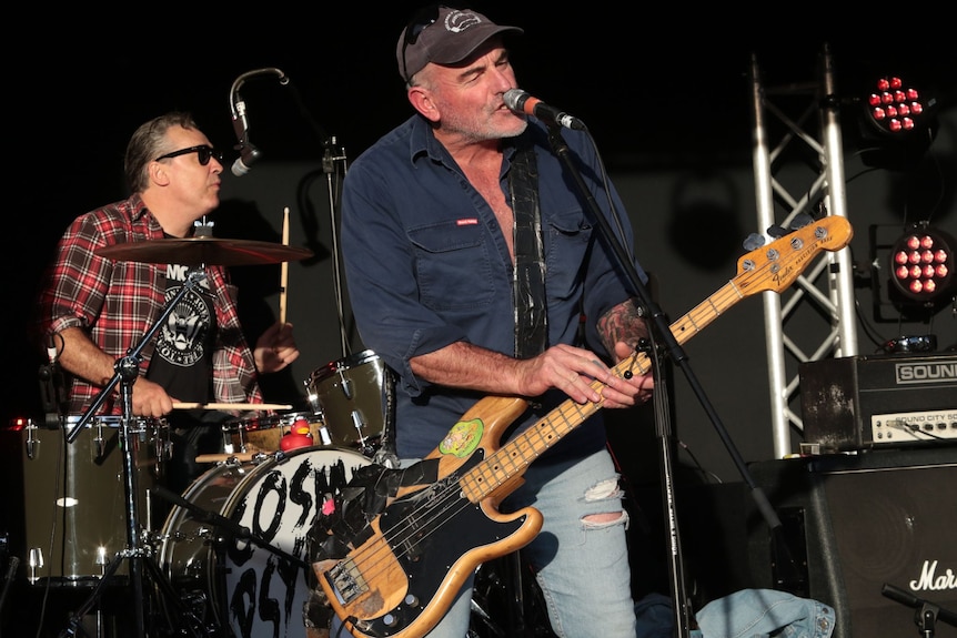 Bass player and drummer in full flight on a small outdoor stage.