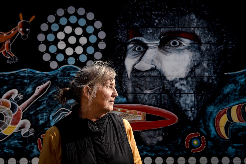 A older woman with an aboriginal mural in the background.