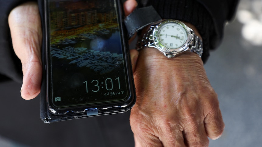 Two hands are pictured, one holds a phone, the other wears a watch. There is a one hour time difference between the two.