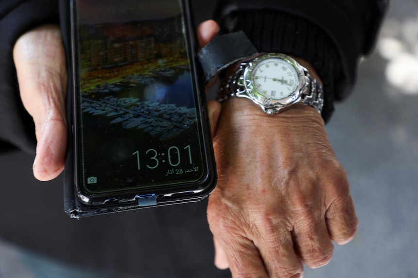 Two hands are pictured, one holds a phone, the other wears a watch. There is a one hour time difference between the two.