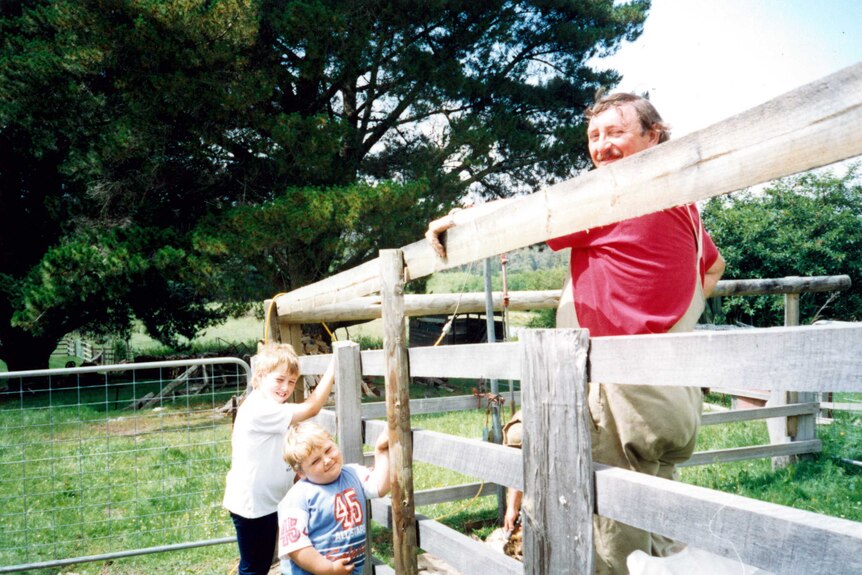 An old photo of Malcolm Wolfe standing on a fence with his sons, Tom and Nick Wolfe.