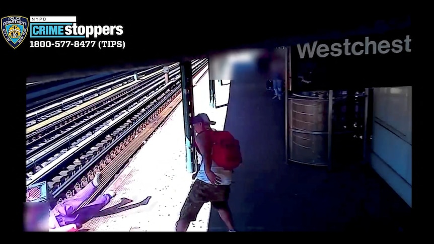 A still from a video shows a man wearing shorts with a red backpack throwing a woman onto train tracks