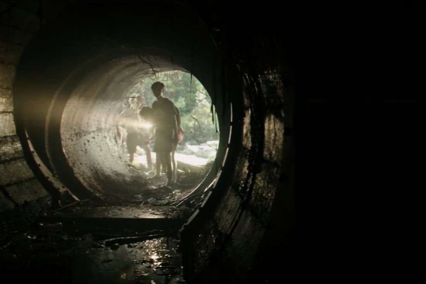 Still image from 2017 film It of the main protagonists shining a torch into an ominous and dark drain pipe.