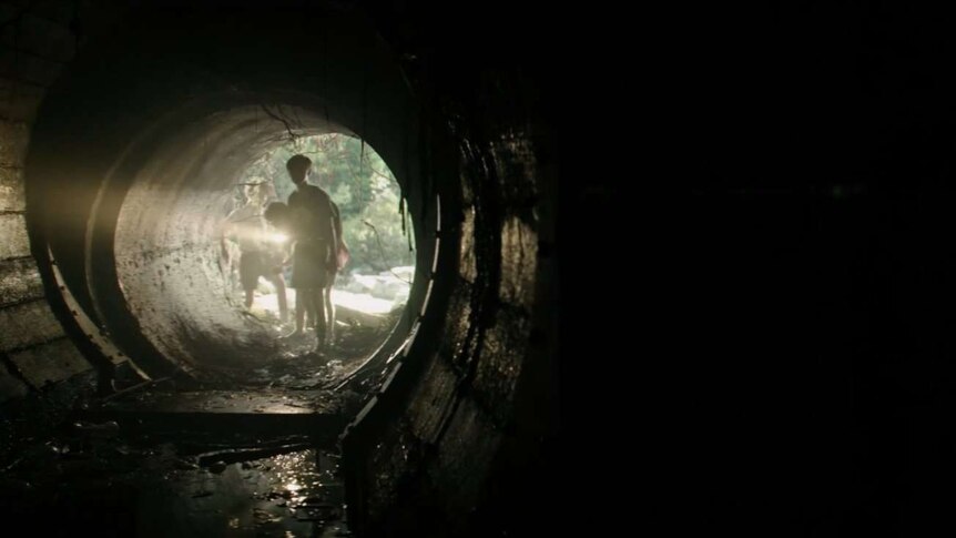 Still image from 2017 film It of the main protagonists shining a torch into an ominous and dark drain pipe.