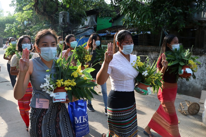 Women carry flowers and do three-finger salutes. 