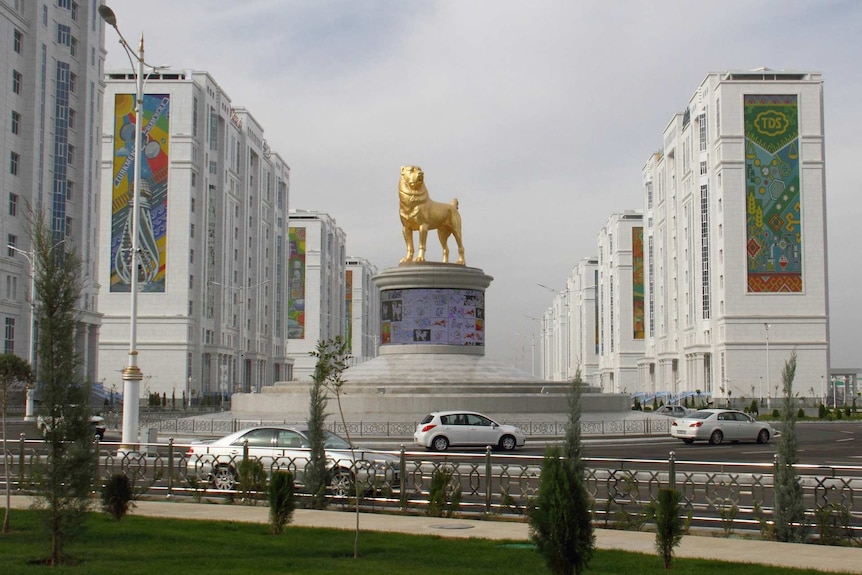 a golden statue of a dog sits on a pedestal in the middle of a roundabout with buildings around it