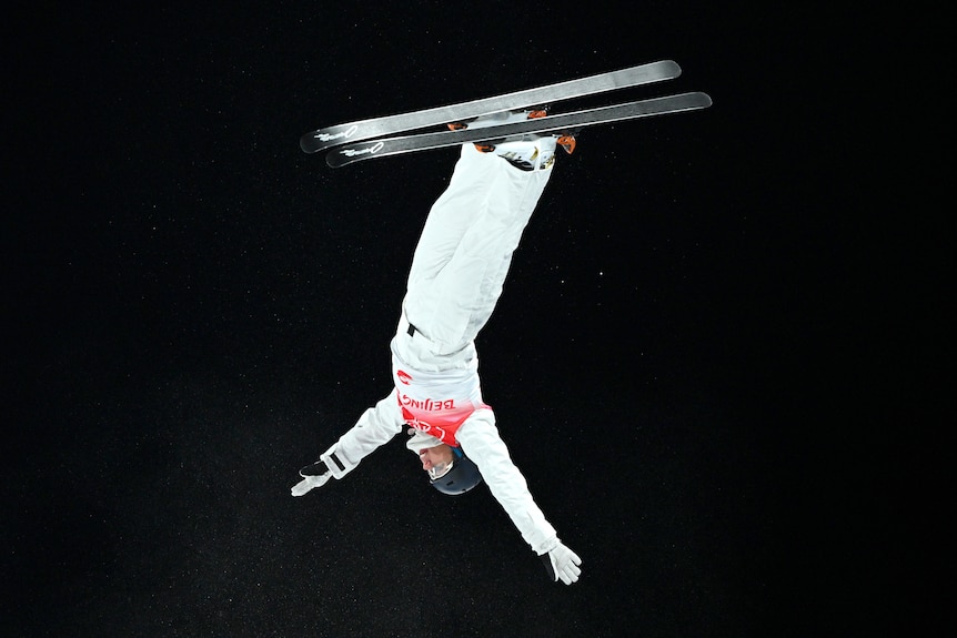 Aeirial skier is upside down completeing a backflip at the Olympic Games.
