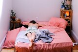 Person lays in unmade bed alone