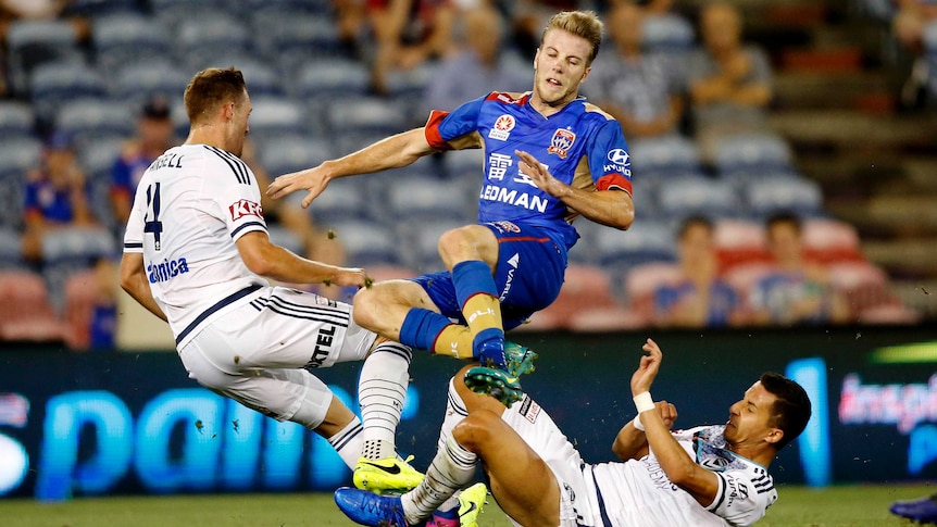 Andrew Hoole gets crunched by two Melbourne Victory players