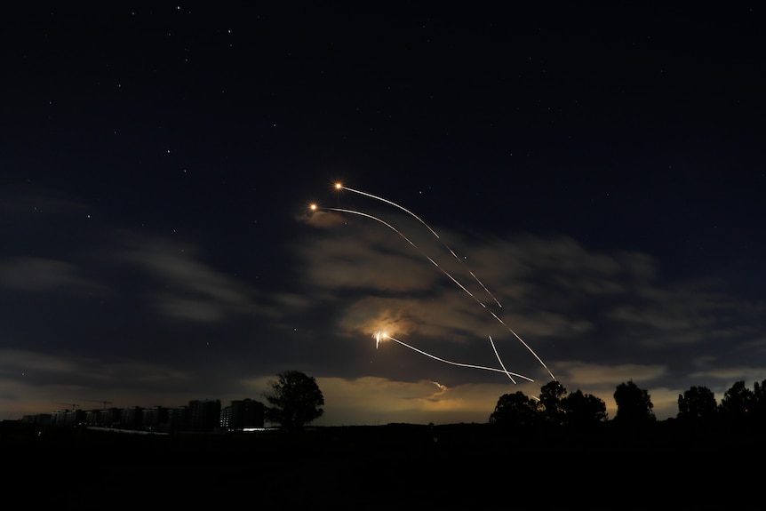 Three flares are flying over a night sky.