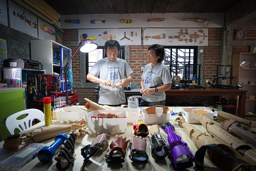 Two people stand behind a table with prosthetics lined up on it