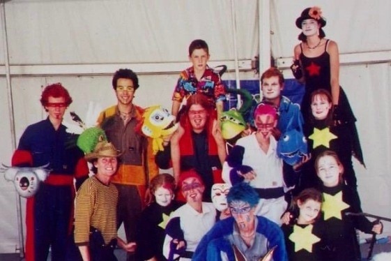 A group of young circus performers in colorful costumes and face paint.