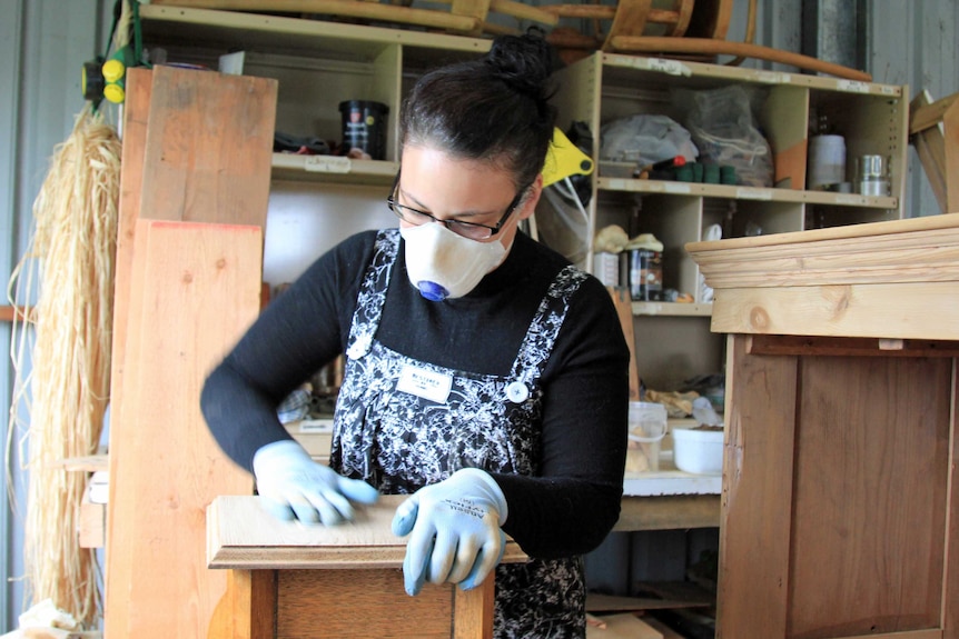 Woman wearing a breathing mask hand-sanding a piece of wooden furniture