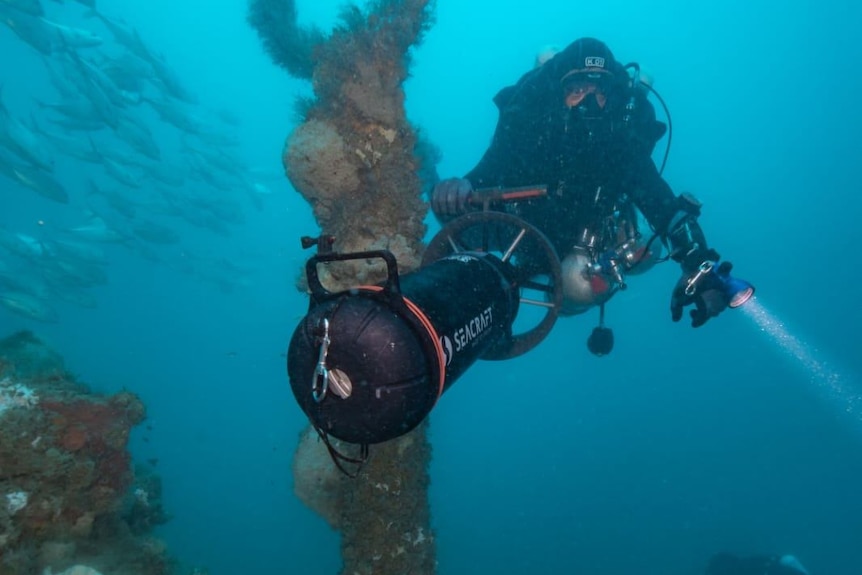 A diver passes by a portion of a sunken submarine with coral growing on it
