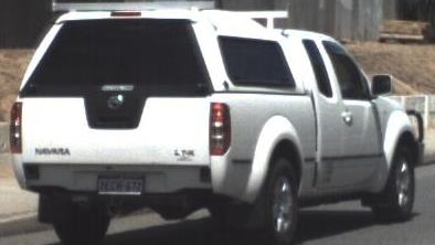 A white 2009 Nissan Navara with a cab drives along a road, viewed from the rear.