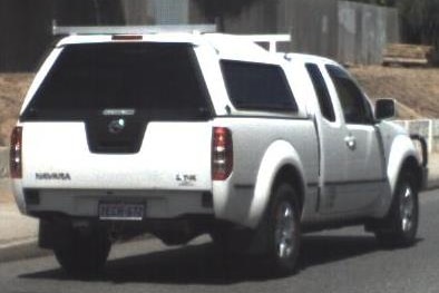 A white 2009 Nissan Navara with a cab drives along a road, viewed from the rear.