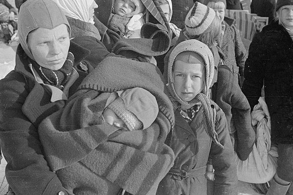 A group of children wearing coats and beanies carry a baby.