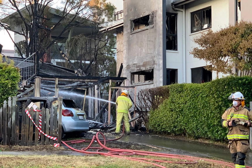 Two fire fighters use a hose to put out fire in a blackened home.