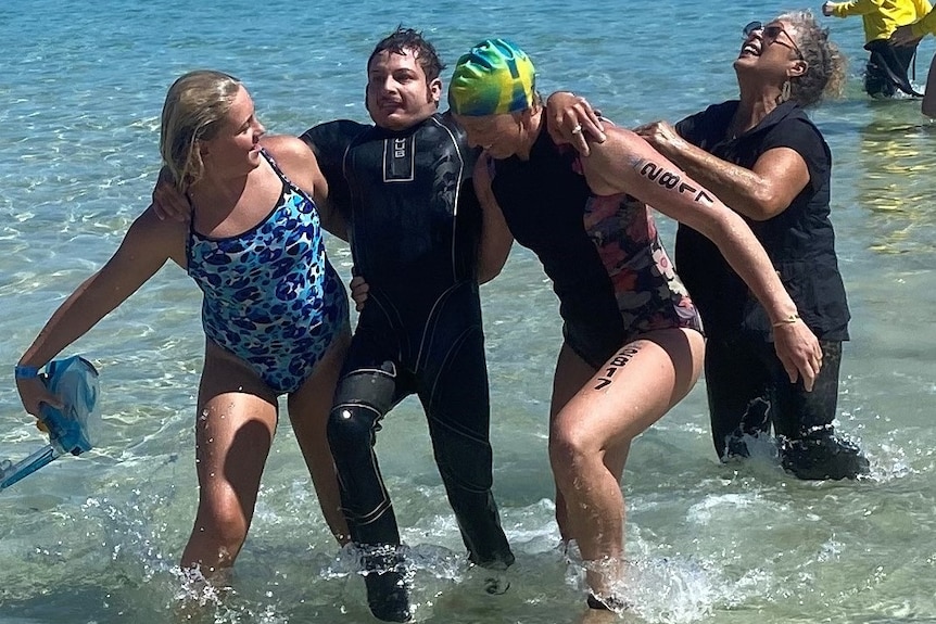A swimmer in a wet suit. He is supported by two other swimmers.