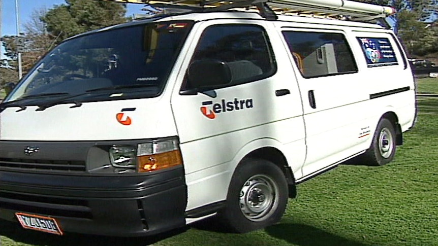 A Telstra work van from the mid-1990s with a ladder on the roof parked on a lawn.