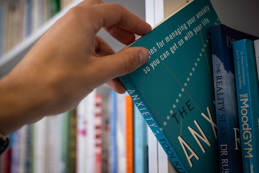 A person pulls a book with the word anxiety on it from a shelf. 