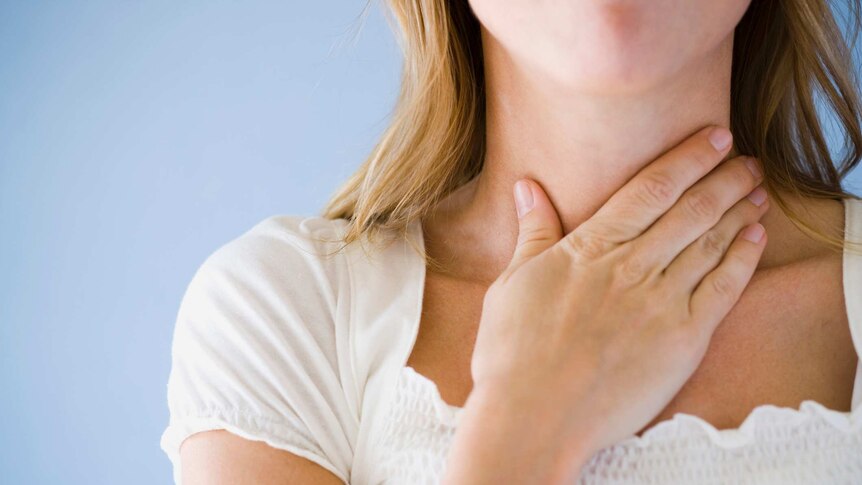 Close-up of a woman with her hand on her throat.