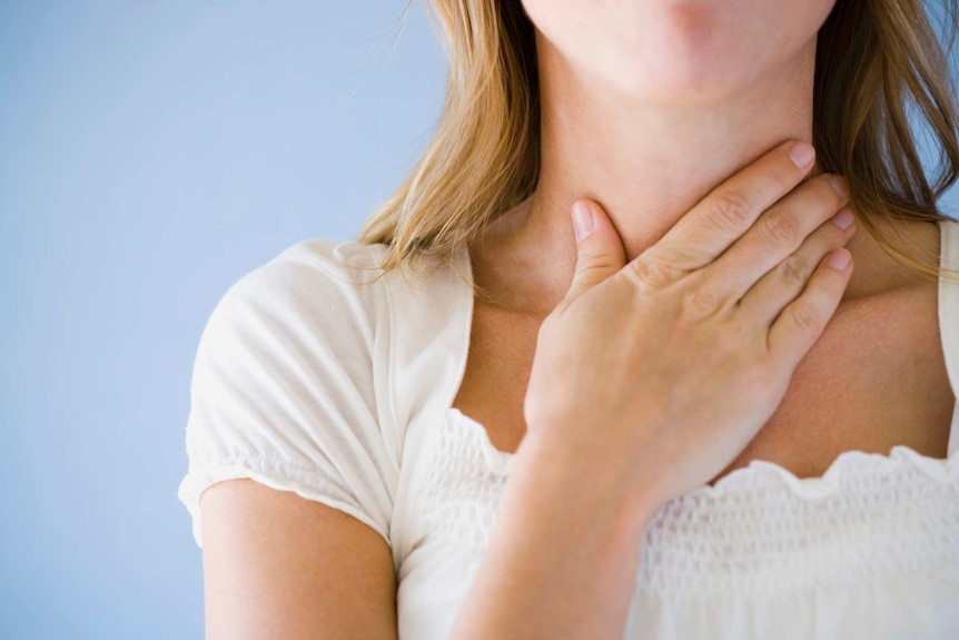 Close-up of a woman with her hand on her throat.