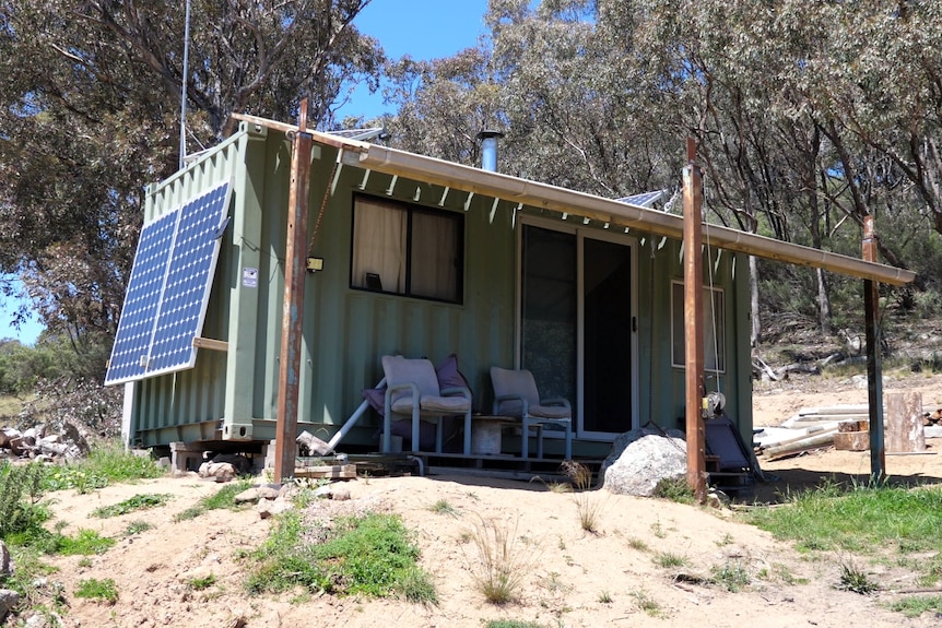 A shipping container fitted out with a wood fire, solar panels, verandah and furniture.