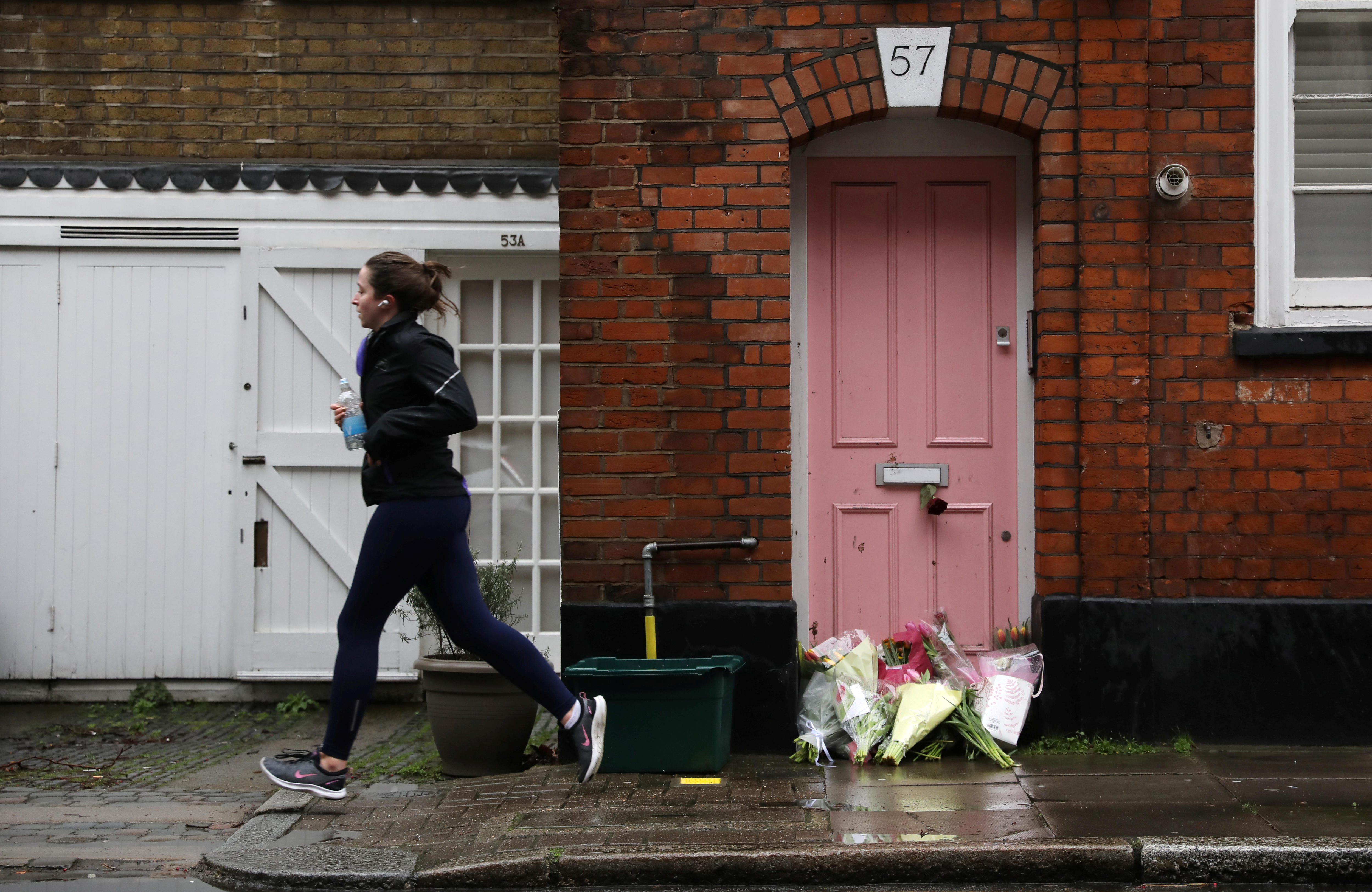 A woman jogs past a pink door with flower bouquets outside it.