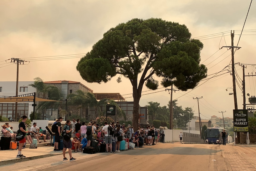 Un grup de turiști așteaptă la drum cu bagajele, sperând să fie transportați din Rodos